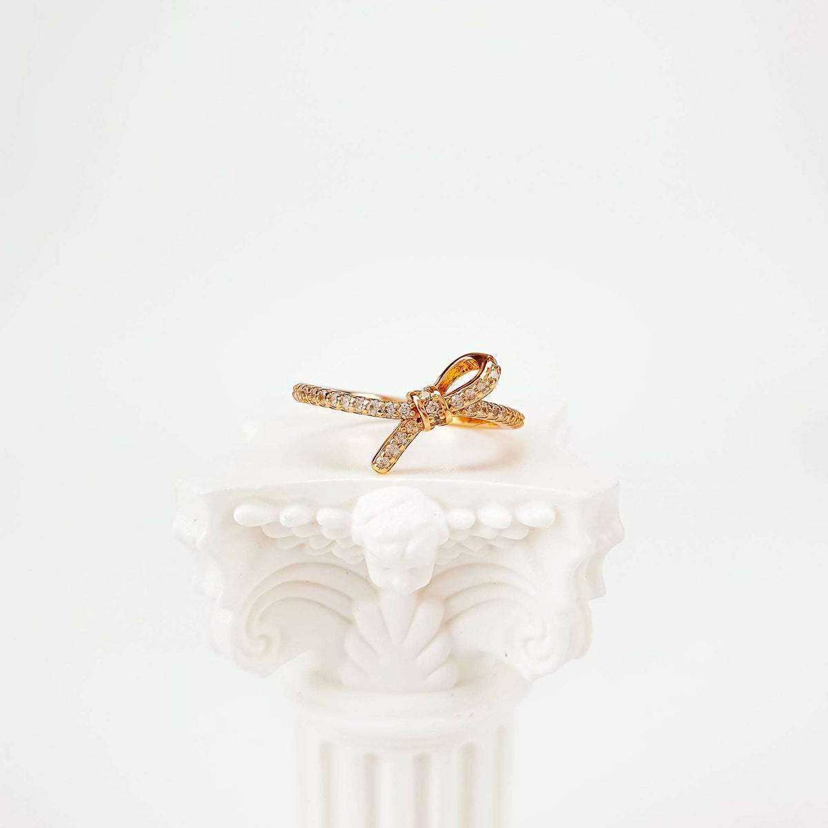 Gold-tone knot ring on a white column stand, view from above