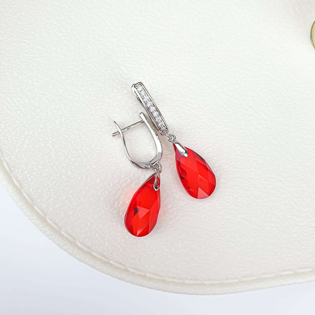 Pair of silver-tone earrings with red teardrop crystals on a light leather background