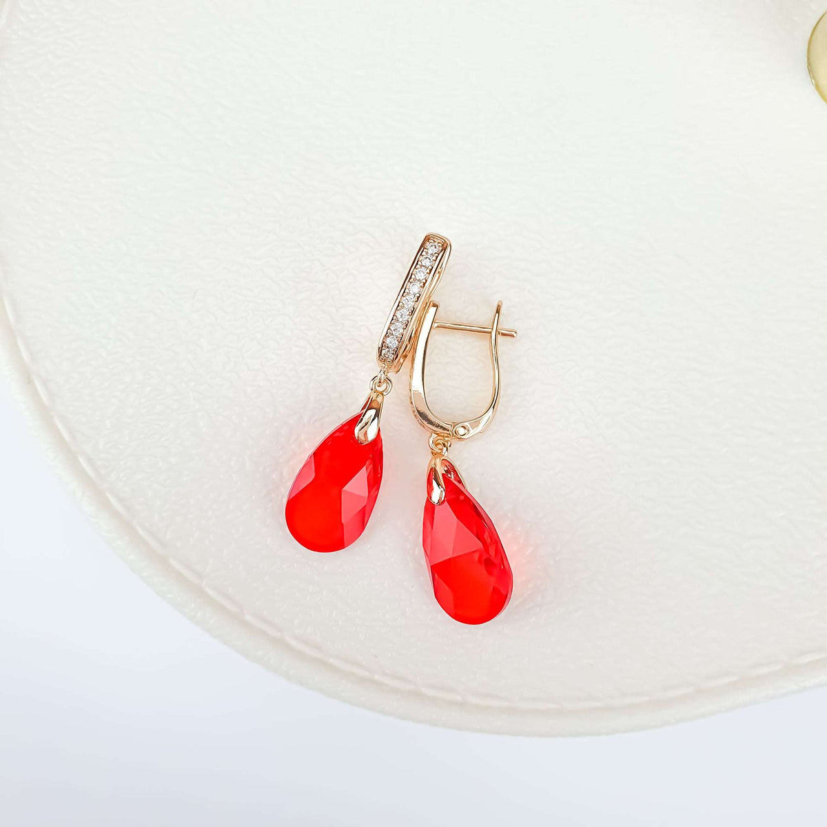 Pair of gold-plated earrings at an angle with red crystals and leverback clasps