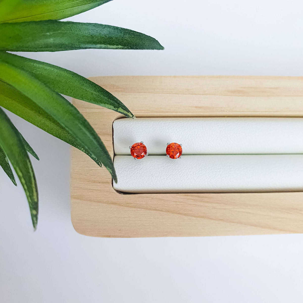 Orange-red sparkling crystal studs on a pale tray beside green leaves