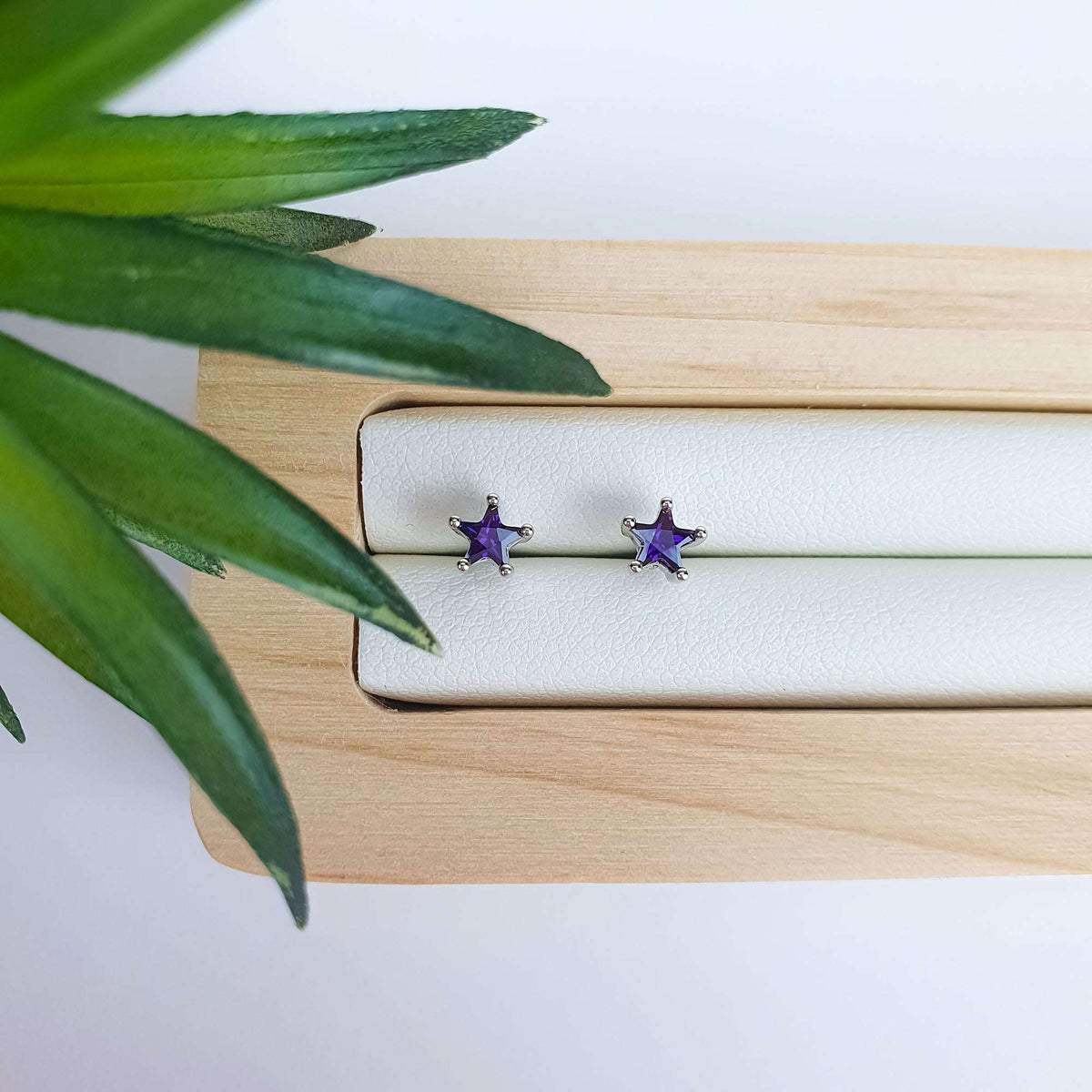 Star studs with bright violet crystals in silver tone on a wooden tray