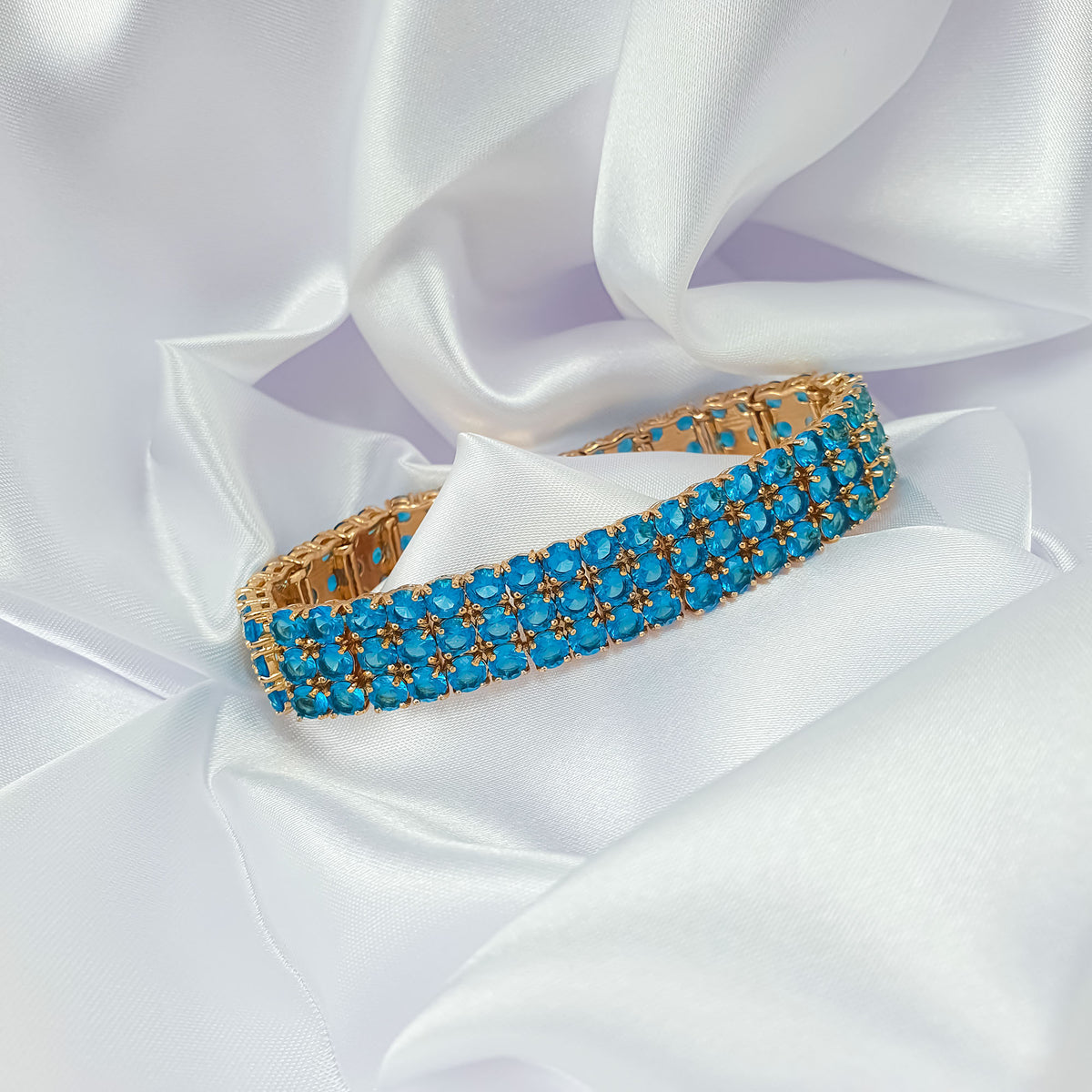 Wide gold-tone bracelet with three rows of bright blue stones on satin