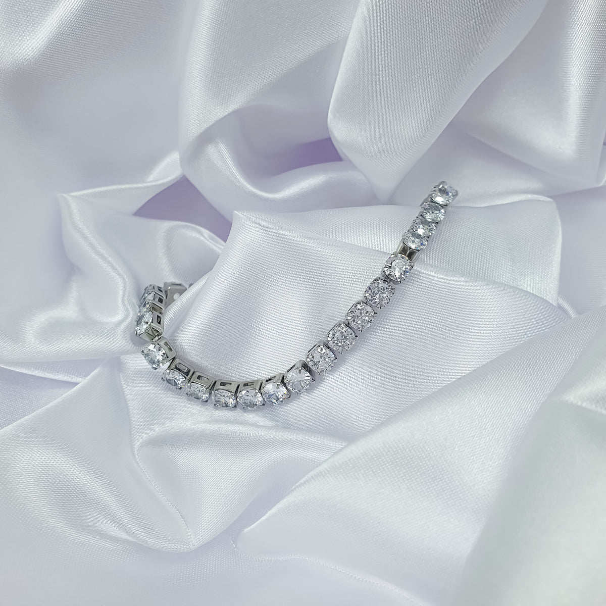 Silver-tone tennis bracelet draped over white satin, sparkling cubic zirconia