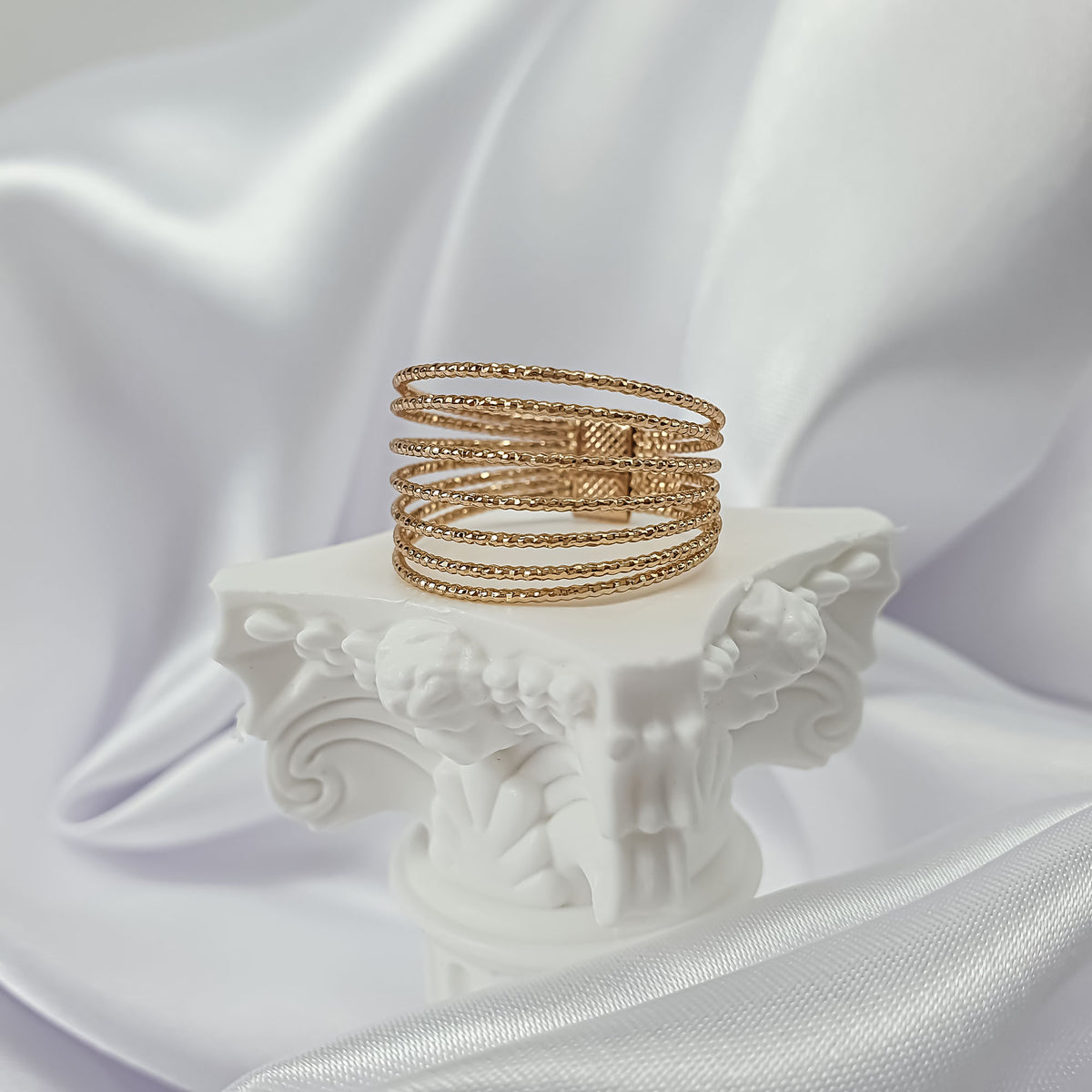 Chunky gold-tone ring with several twisted rows on a white column