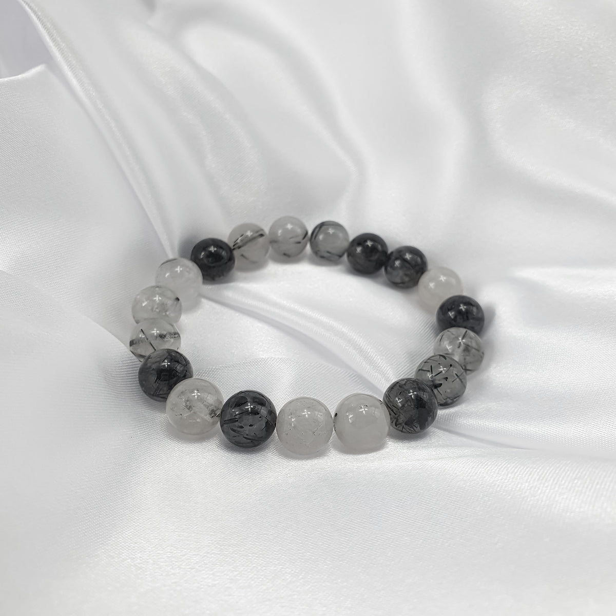 Black and white tourmalinated quartz bracelet on white satin, glossy round beads