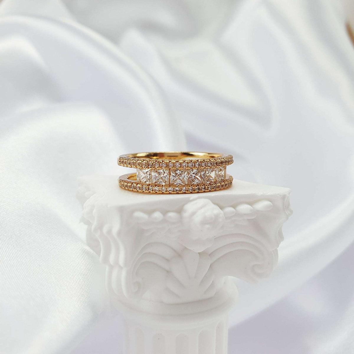 Gold-tone cubic zirconia ring from the side on a white plaster column