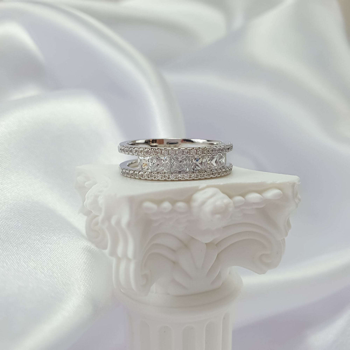 Silver-tone cubic zirconia ring from the side on a white plaster column, silk folds