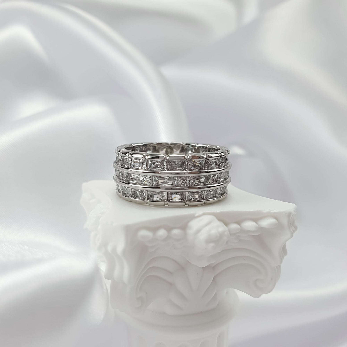 Ring from the front on a white stand, three rows of clear square stones