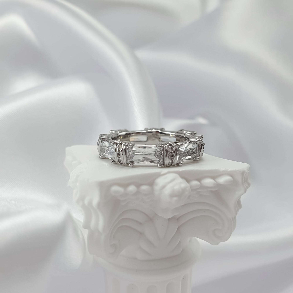Silver-tone cubic zirconia ring on a white plaster column against silk