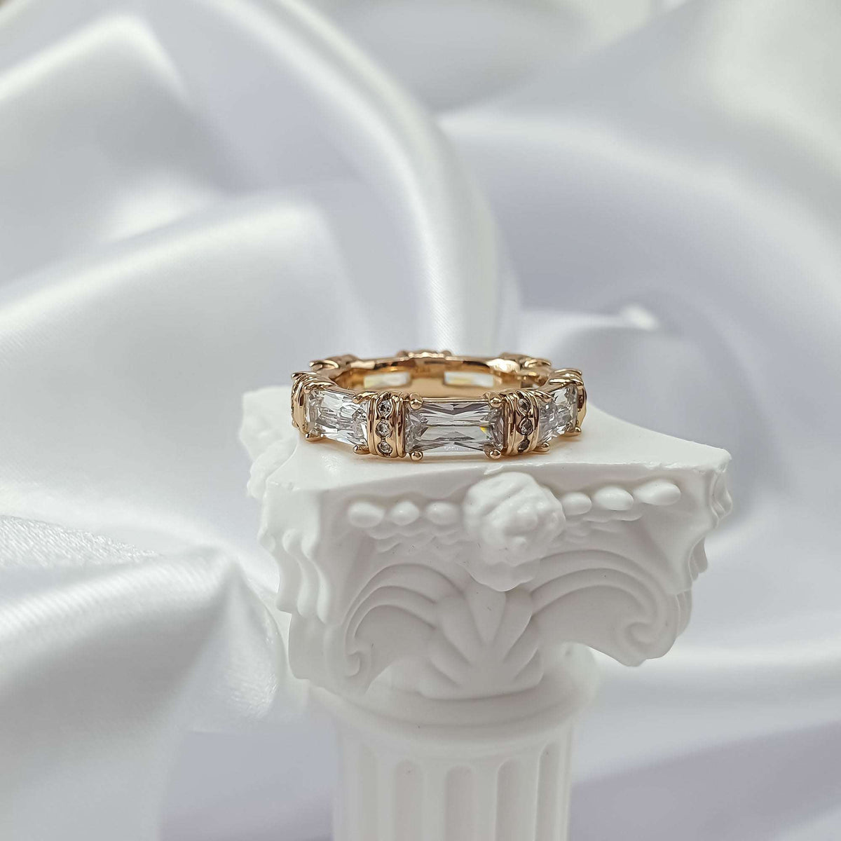 Gold-tone cubic zirconia ring on a white plaster column with silk behind