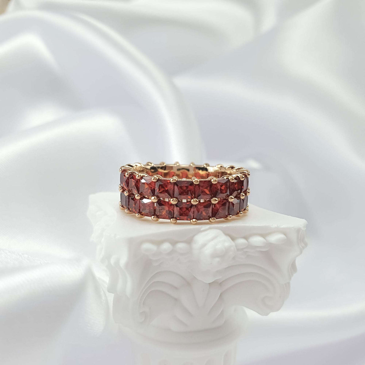 Two-row red cubic zirconia ring on a white column, warm gold-tone finish