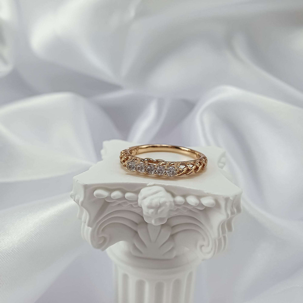 Gold-tone ring with five cubic zirconia on a white plaster column with silk