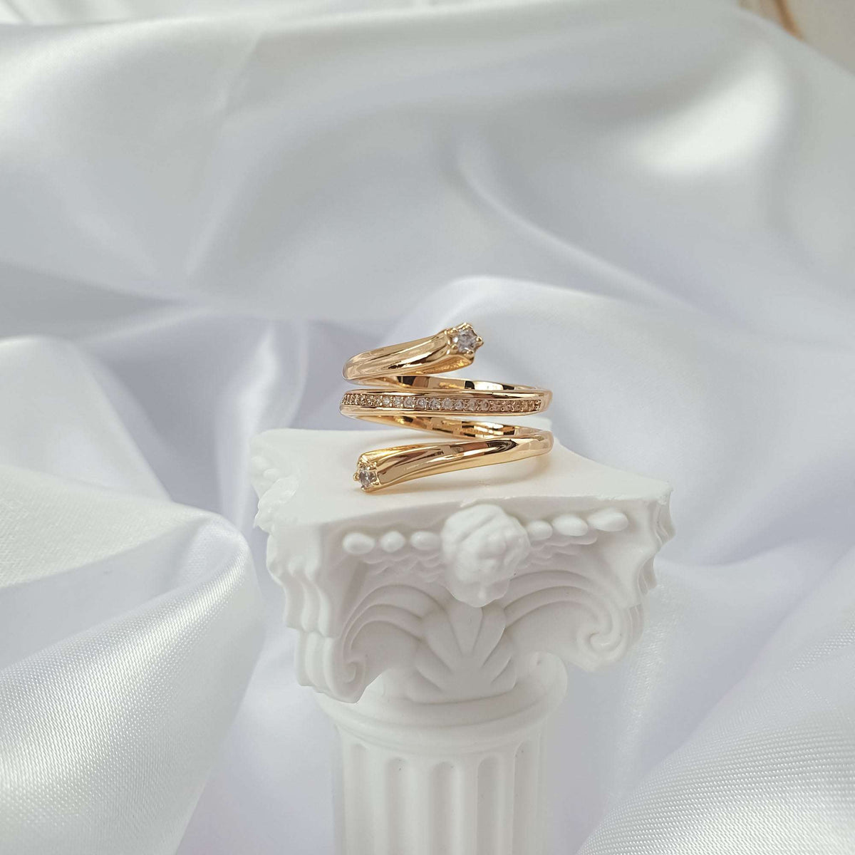 Twisting gold-tone ring with a sparkling row of stones on a white column