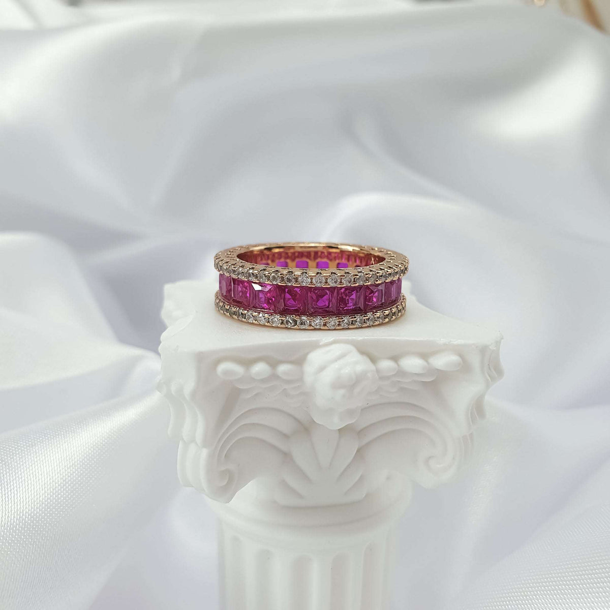 Pink cubic zirconia ring, side view on a white column with silky fabric