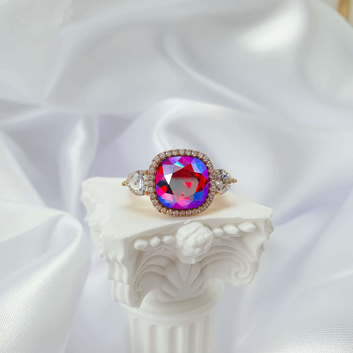 Multicoloured crystal ring with a clear stone halo on a white column
