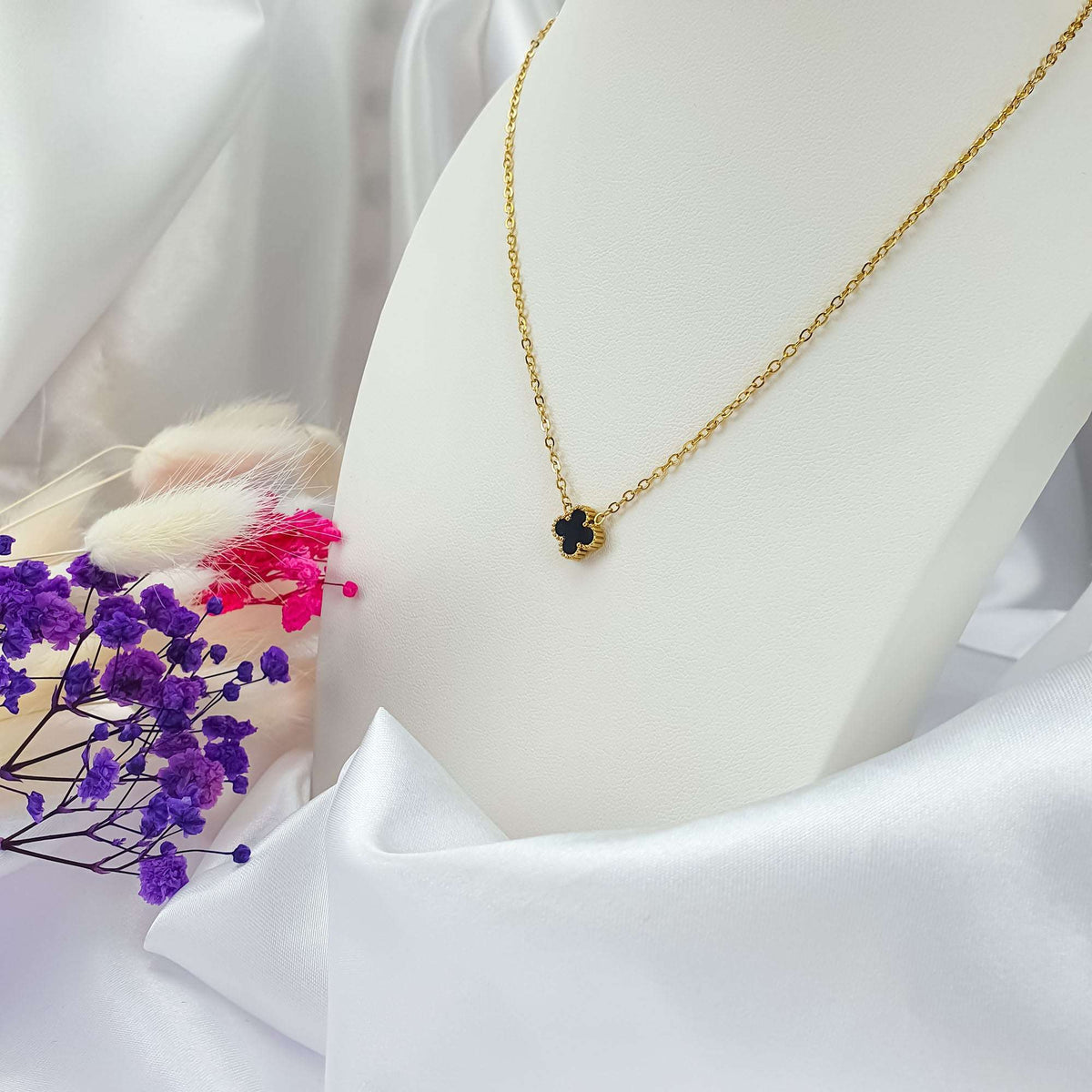 Black four-leaf pendant in a golden frame on a light stand by dried flowers