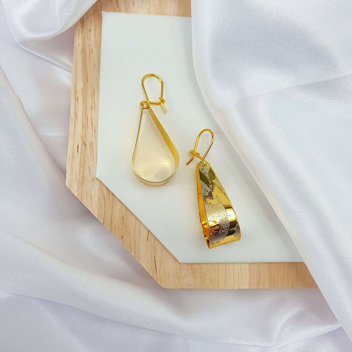 Pair of earrings from the side, one face smooth, one ridged, wooden stand