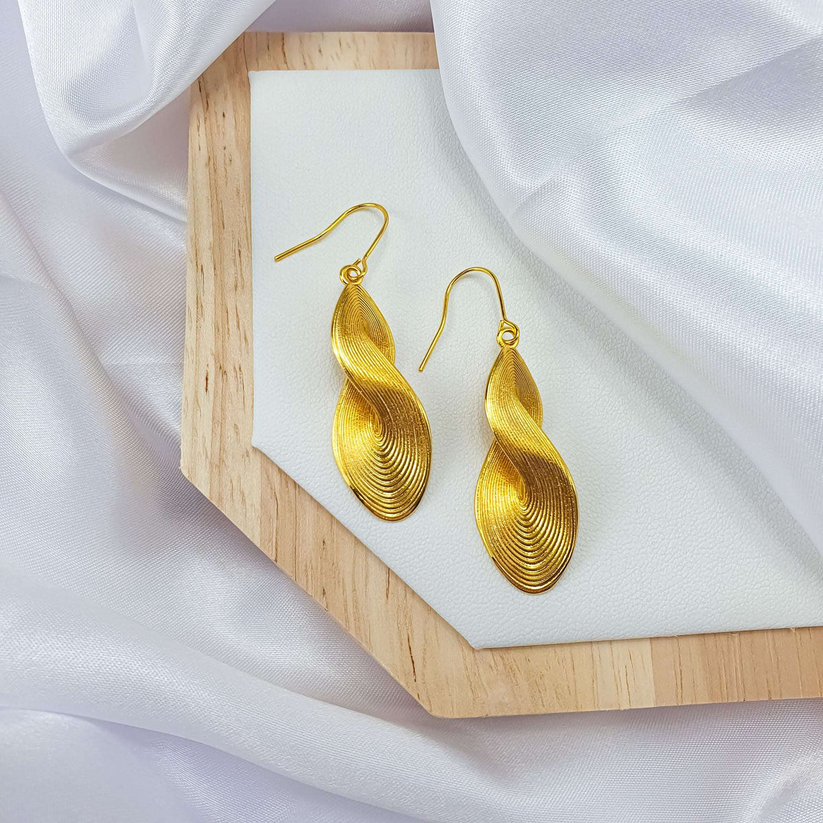 Wavy gold-plated earrings on a wooden stand with white silk