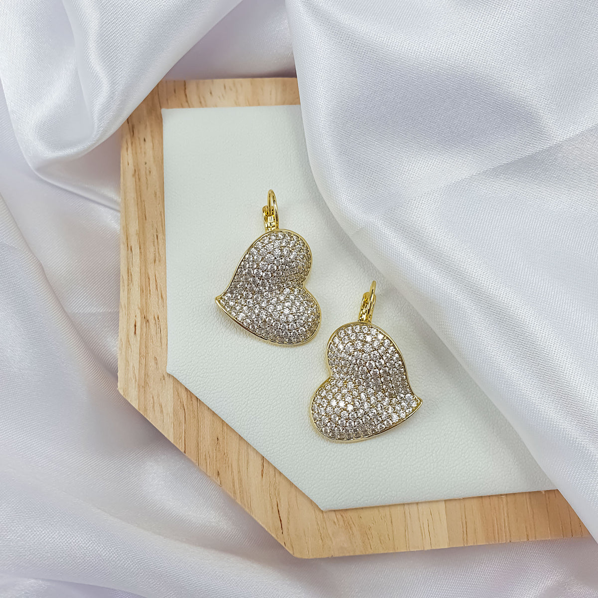 Pair of pavé heart earrings on a wooden stand in white silk