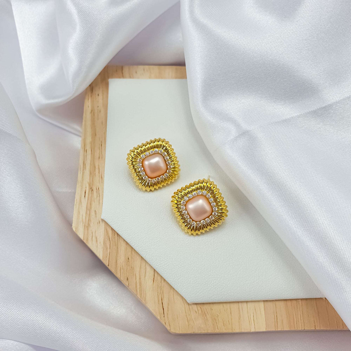 Faux pearl earrings in ribbed gold-plated frames on a wooden stand