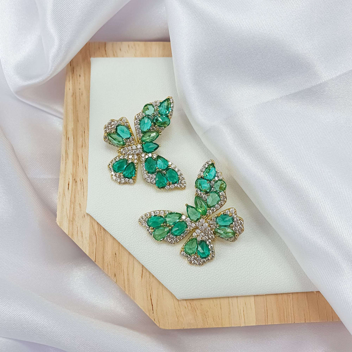 Pair of green butterfly earrings on a wooden stand in white silk