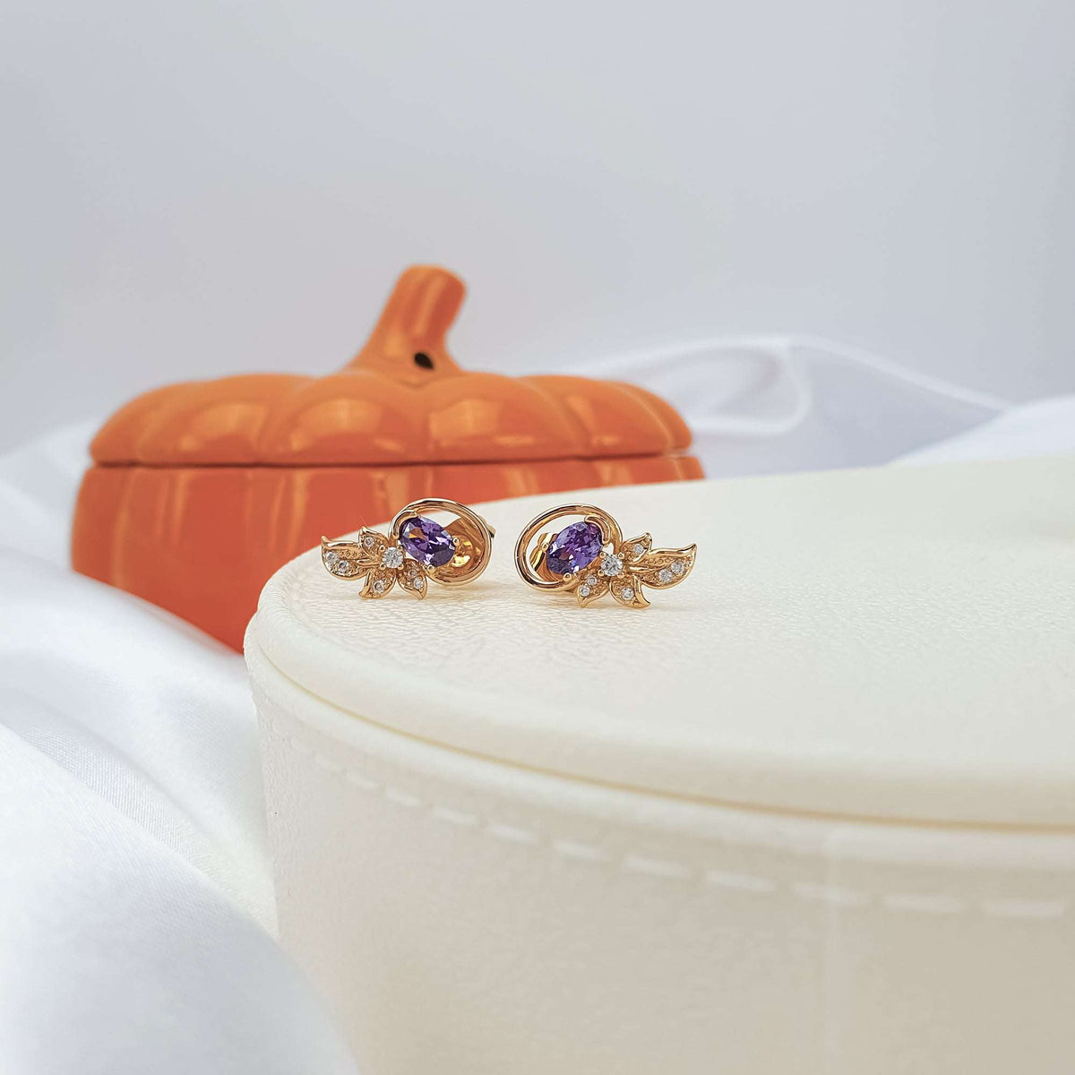 Pair of violet oval studs with sparkling leaves on a light box