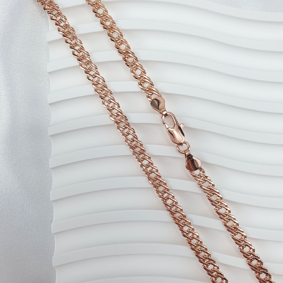 Rose gold tone chain with rhombus links on a white wavy background