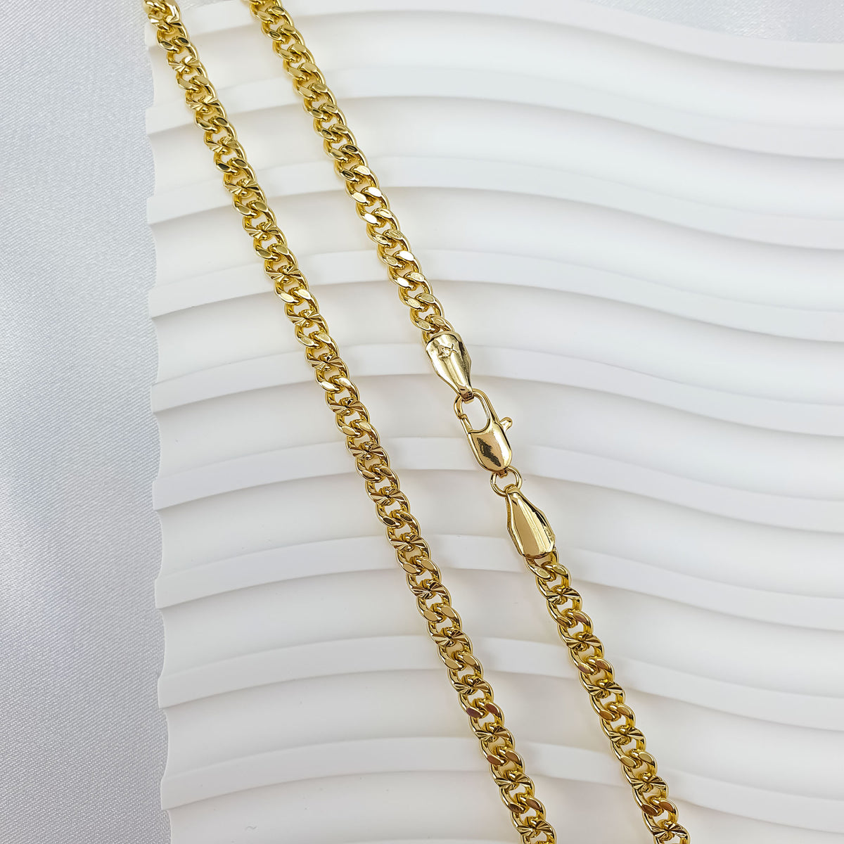 Yellow gold tone chain on a white wavy background, weave texture visible