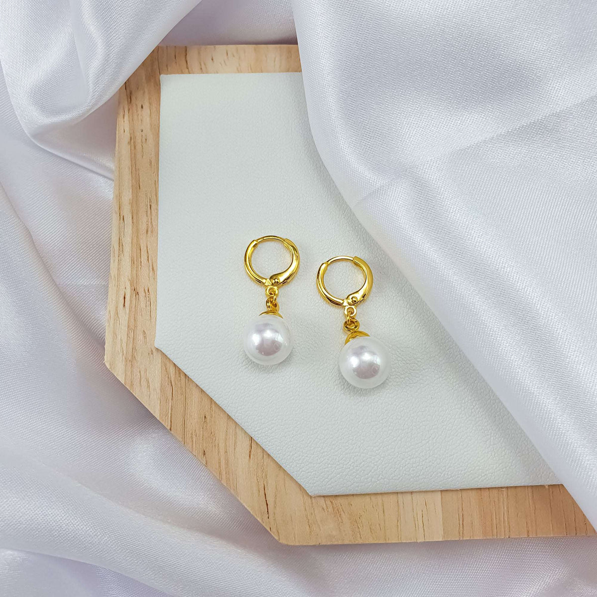 Gold-plated French hook earrings with white faux pearls on a wooden stand