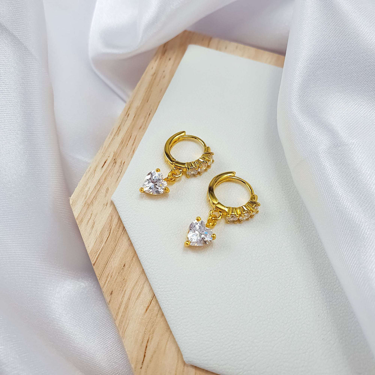 Gold-plated heart earrings with clear zirconia on a wooden stand and silk