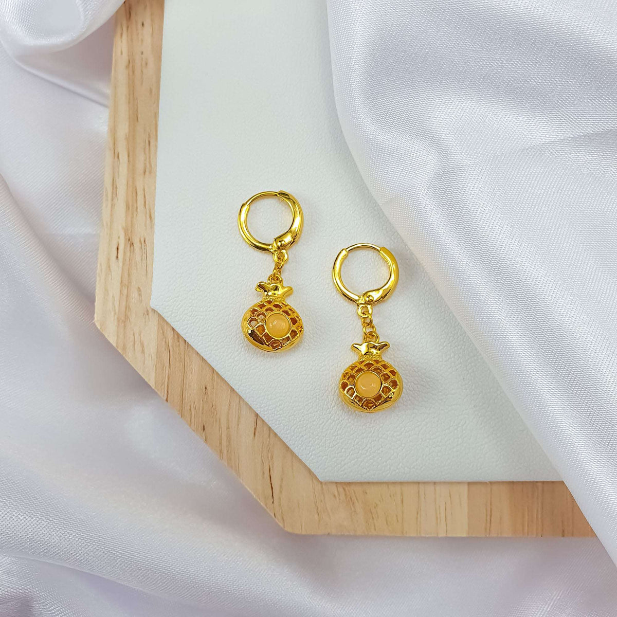 Gold-tone pineapple earrings with cream stones on a wooden board and silk