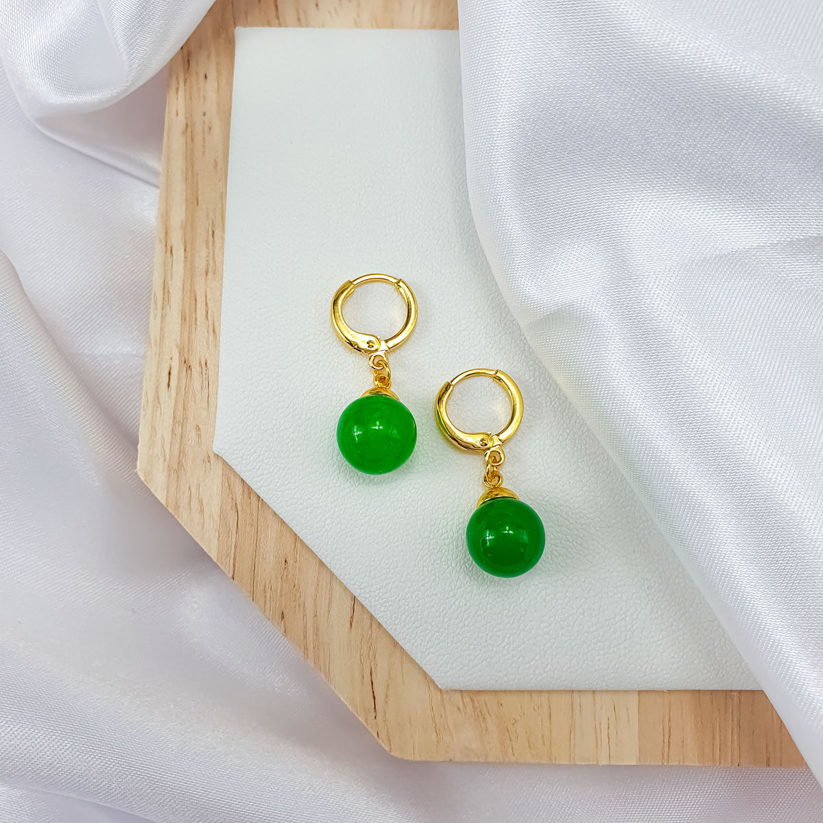 Green bead earrings with gold-plated hoops on a wooden board and white silk