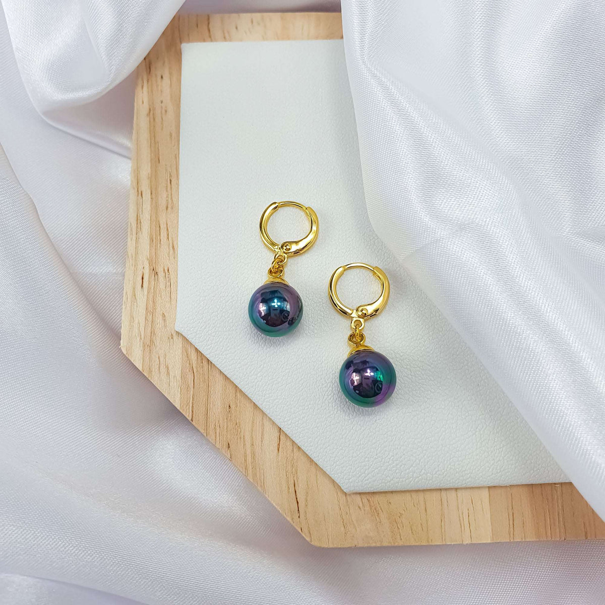 Pair of earrings with blue-black faux pearls on a wooden stand and silk