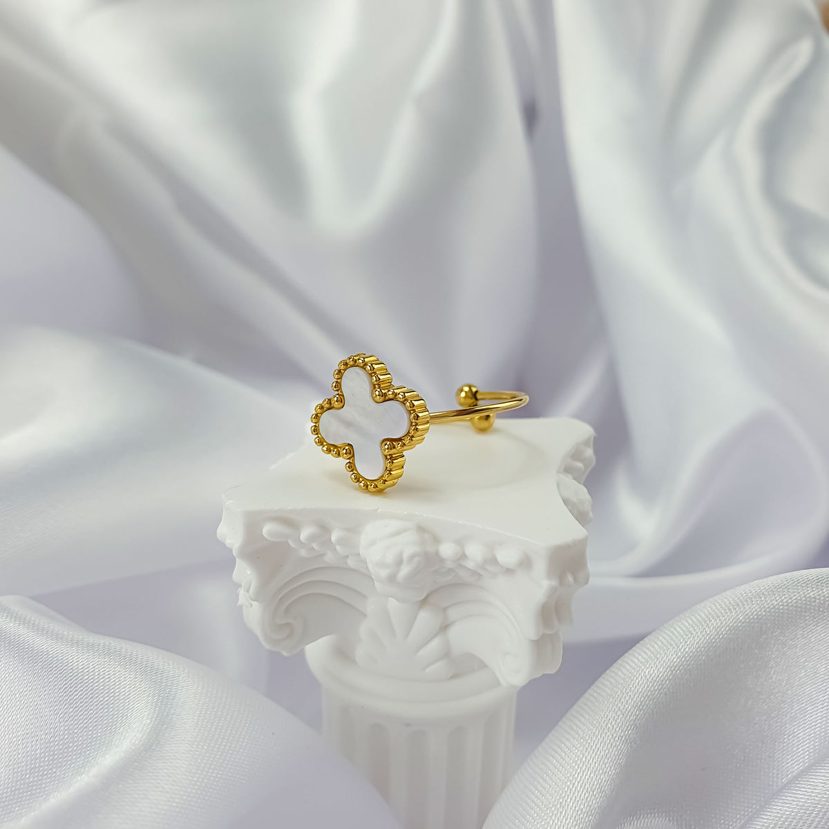 Gold-tone clover ring with an open band on a white column and silk