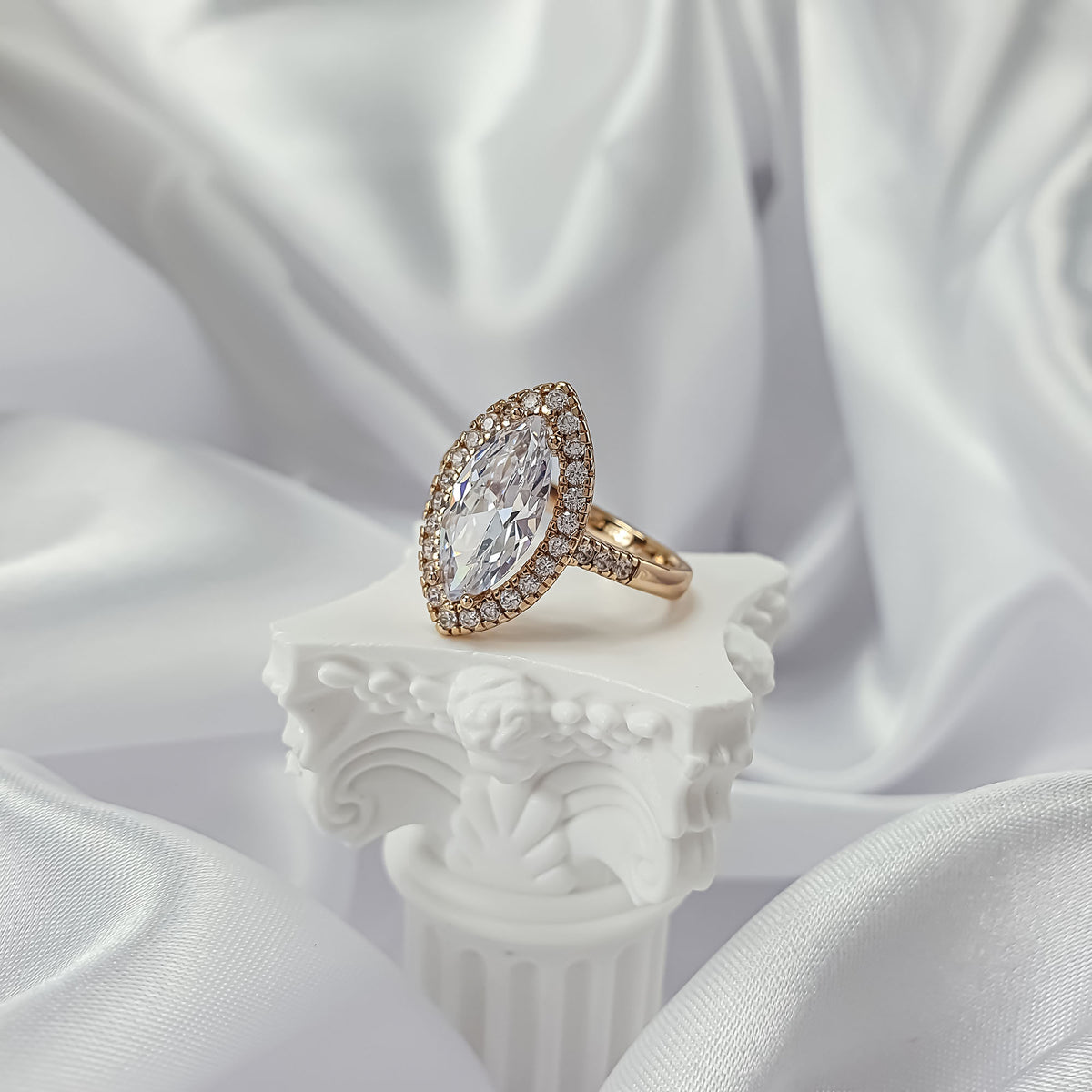 Gold-plated marquise zirconia ring with a clear stone halo on a white stand