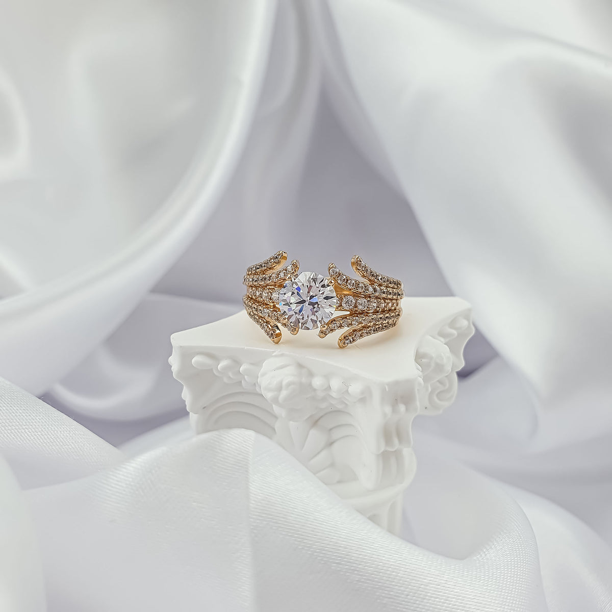 Gold-plated cubic zirconia ring on a white column against silk fabric