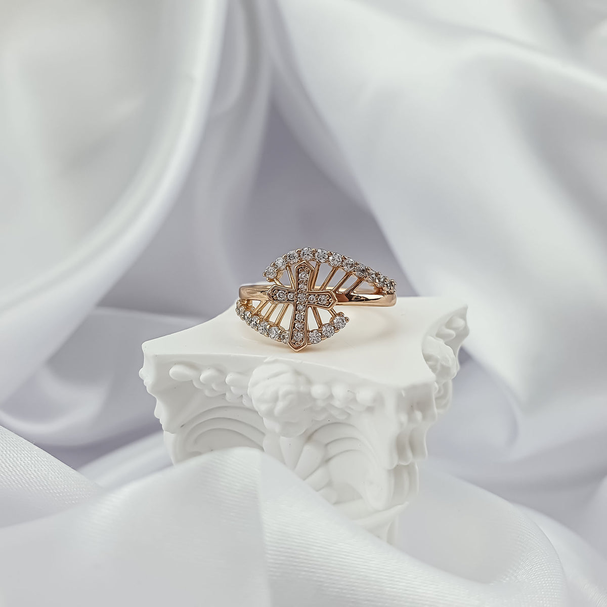 Gold-plated cross ring on a white plaster column with silk fabric