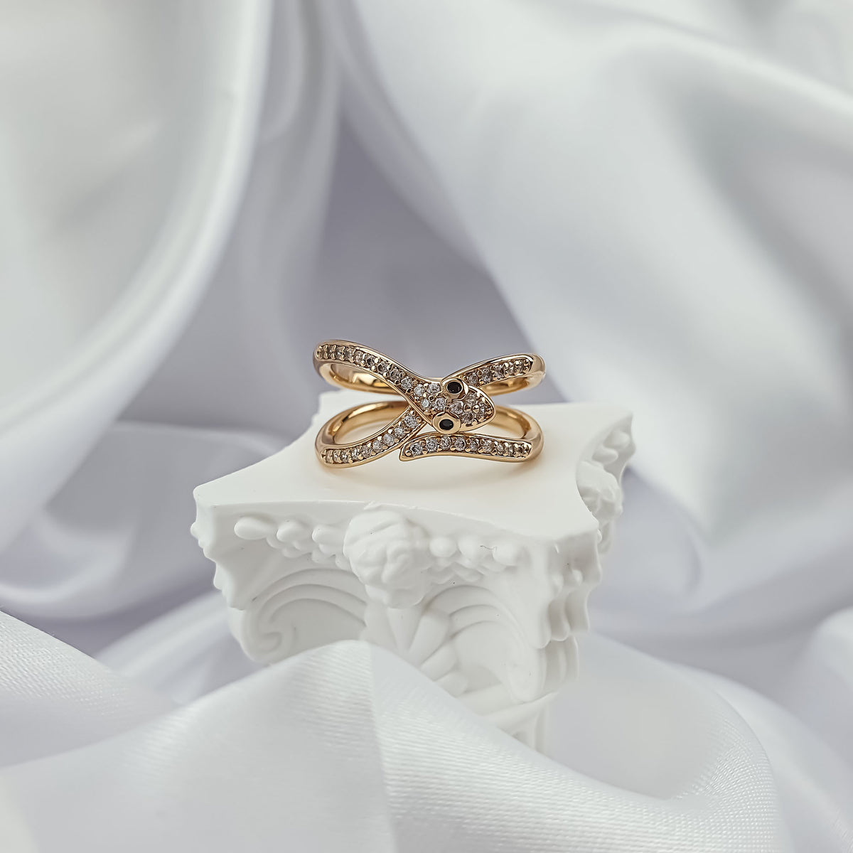 Crossover snake ring with cubic zirconia on a white plaster stand and silk