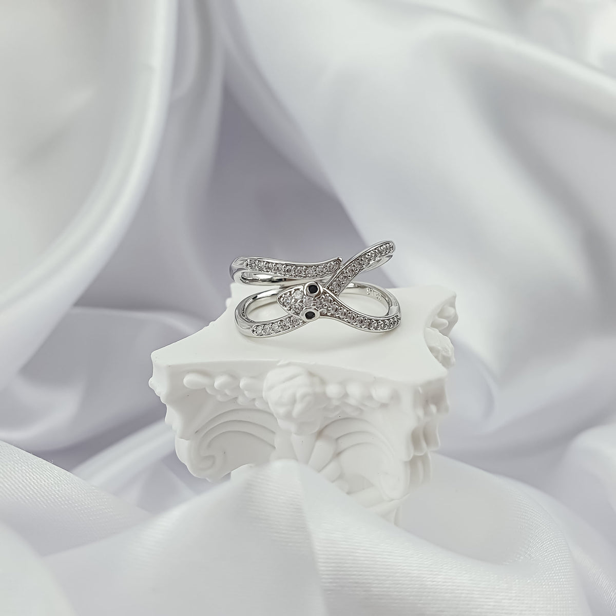 Silver-tone snake ring with clear stones and black eyes on a white stand