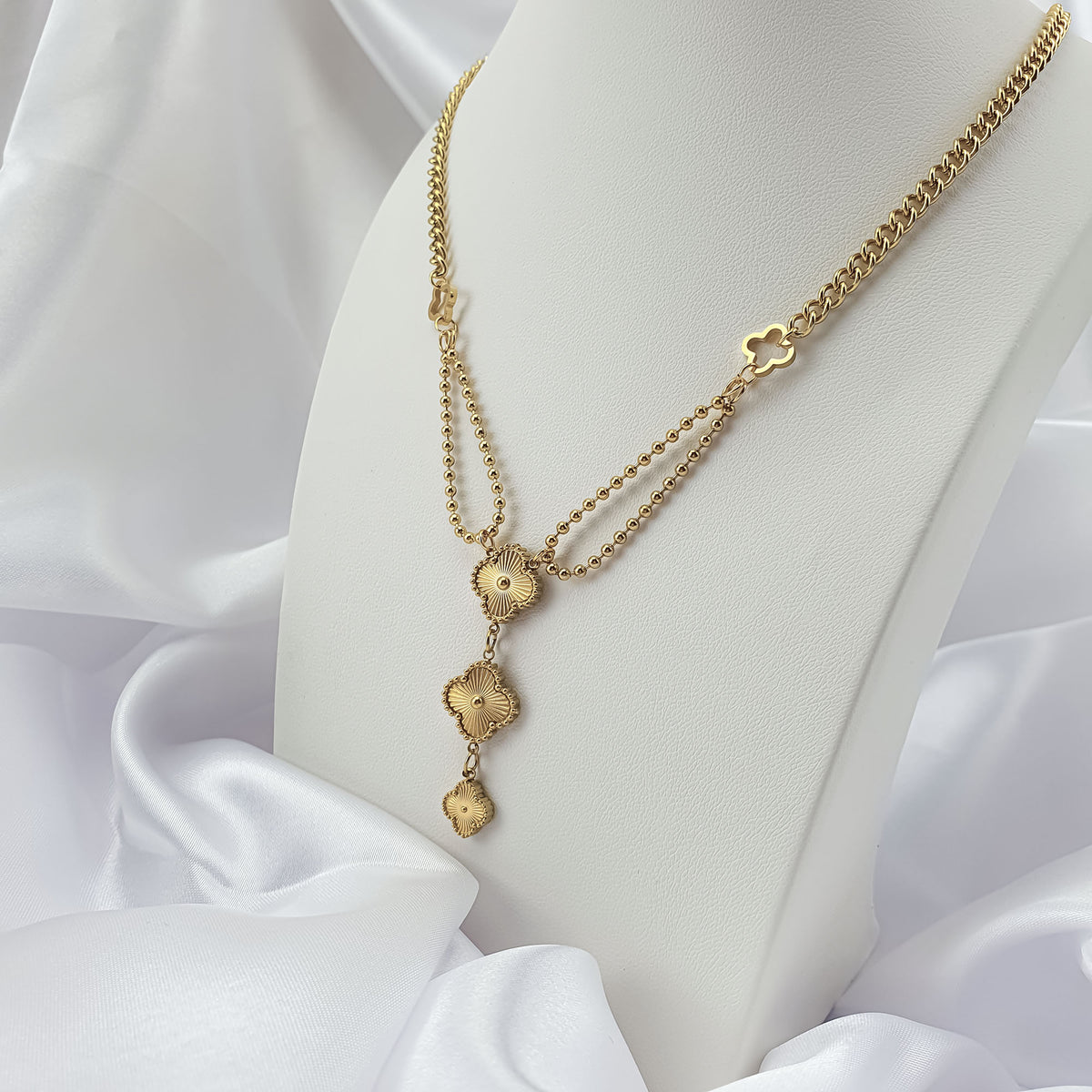 Gold-tone clover necklace on a white stand showing bead and link chains