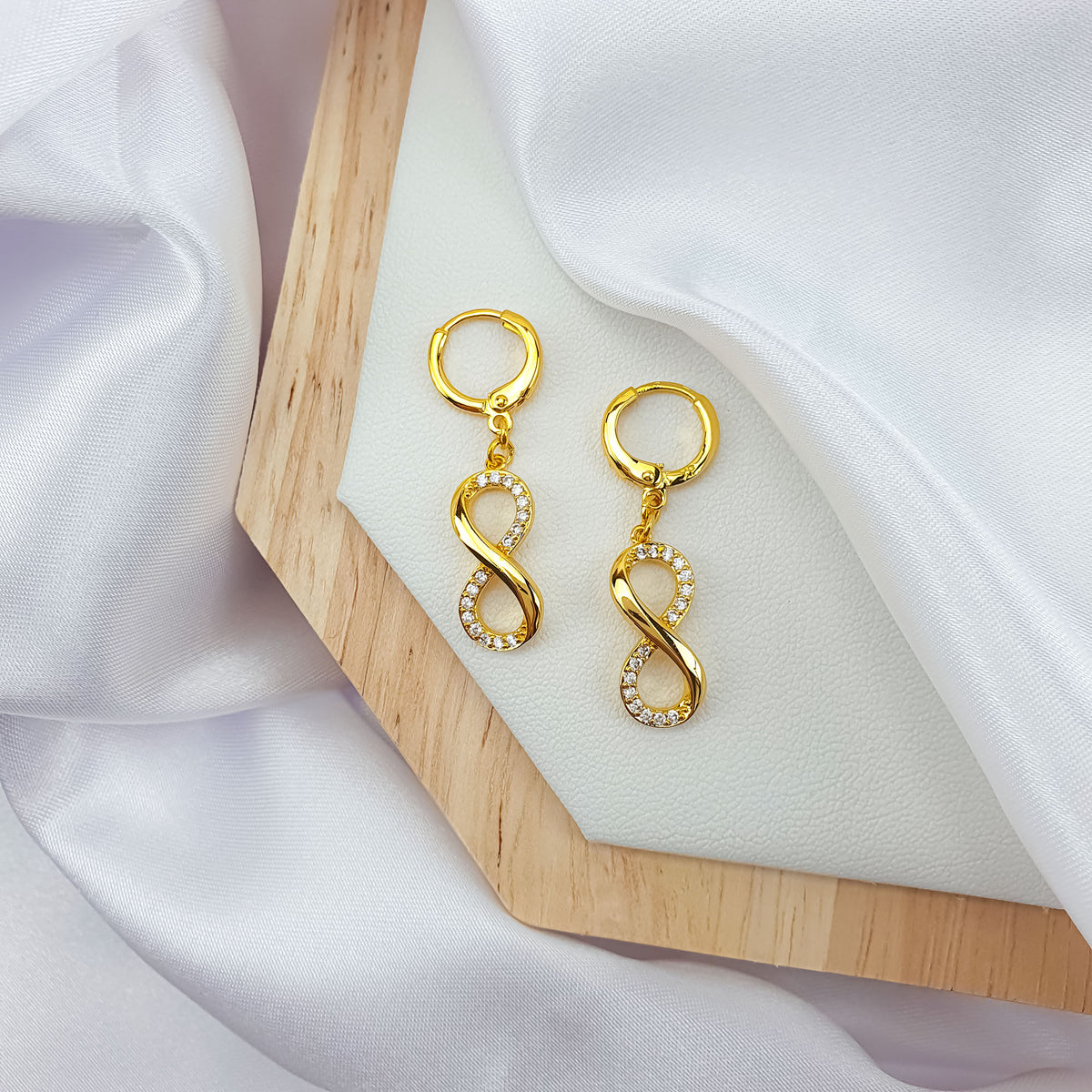 Pair of gold-tone infinity earrings on a wooden tray and white silk
