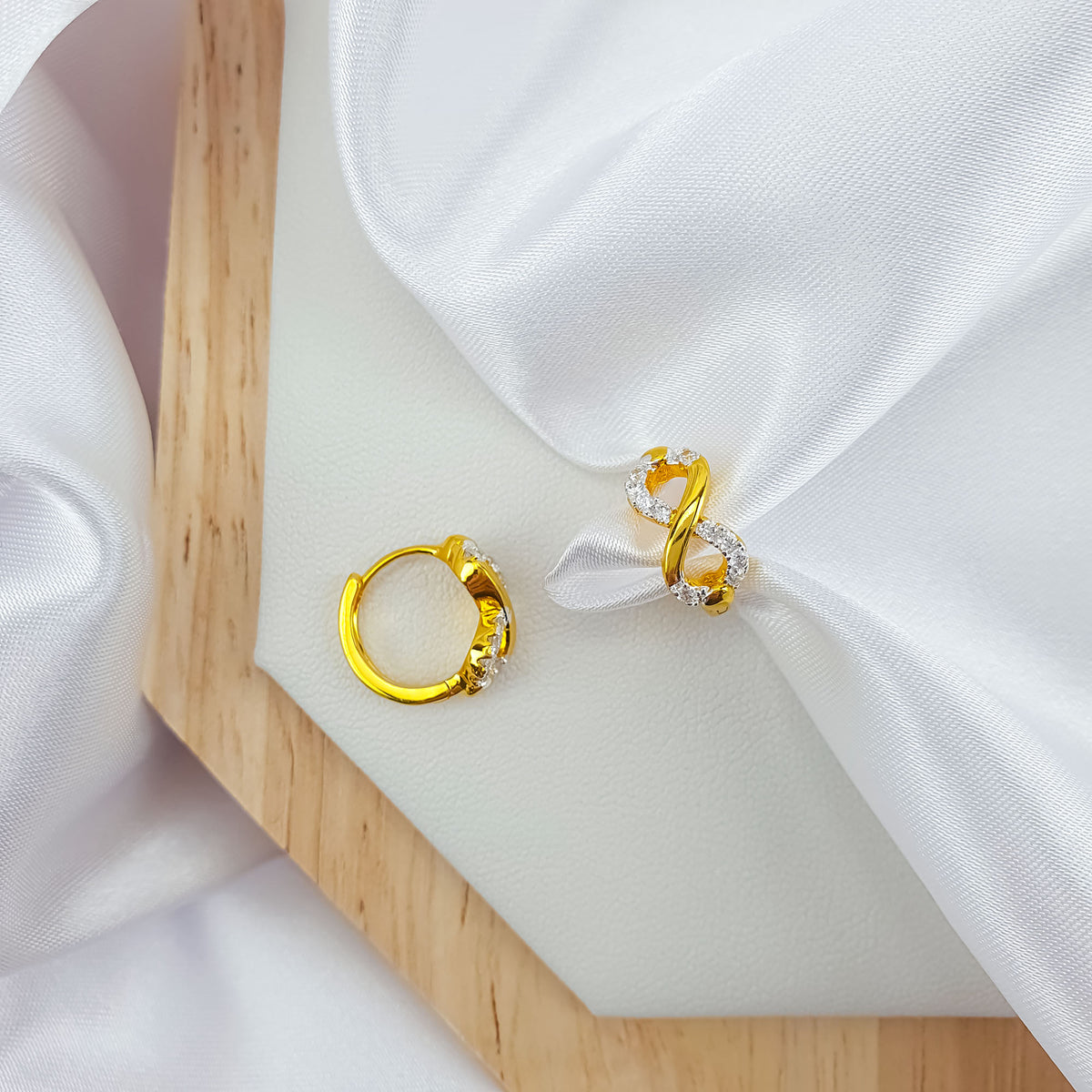 Two gold-tone infinity earrings on white silk showing the round clasp