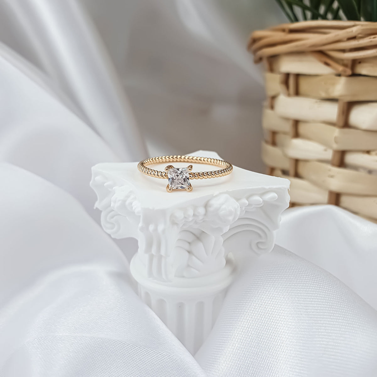 Slim gold-plated ring with a bright square stone on a white column