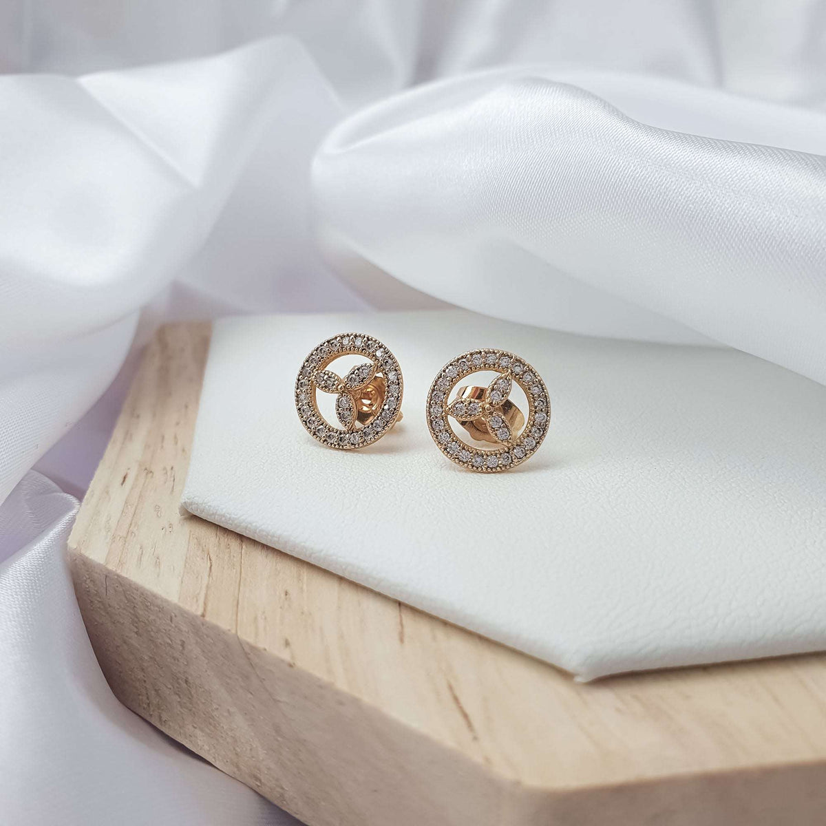Close-up of gold-plated trefoil studs with a cubic zirconia border on a white tray
