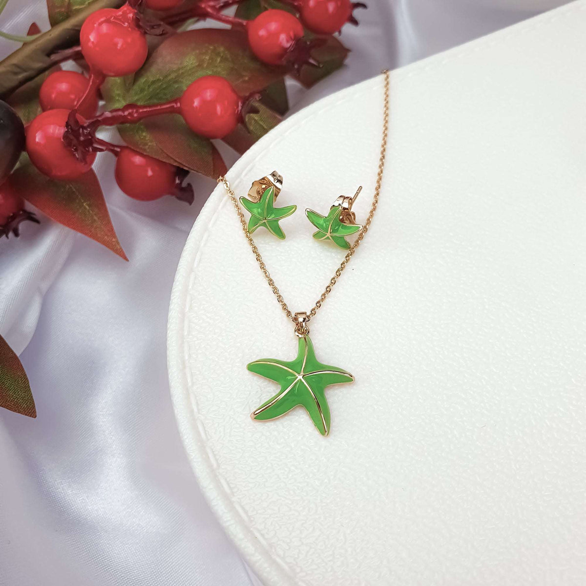 Green enamel starfish set with a gold-plated chain on a white box beside berries