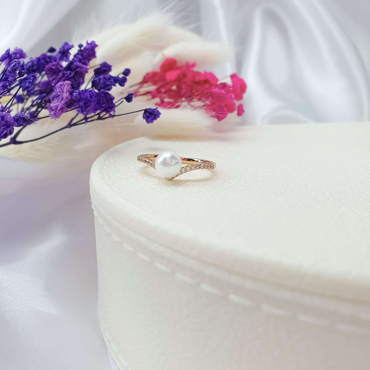 Delicate gold-plated pearl ring with cubic zirconia on a white box among dried flowers