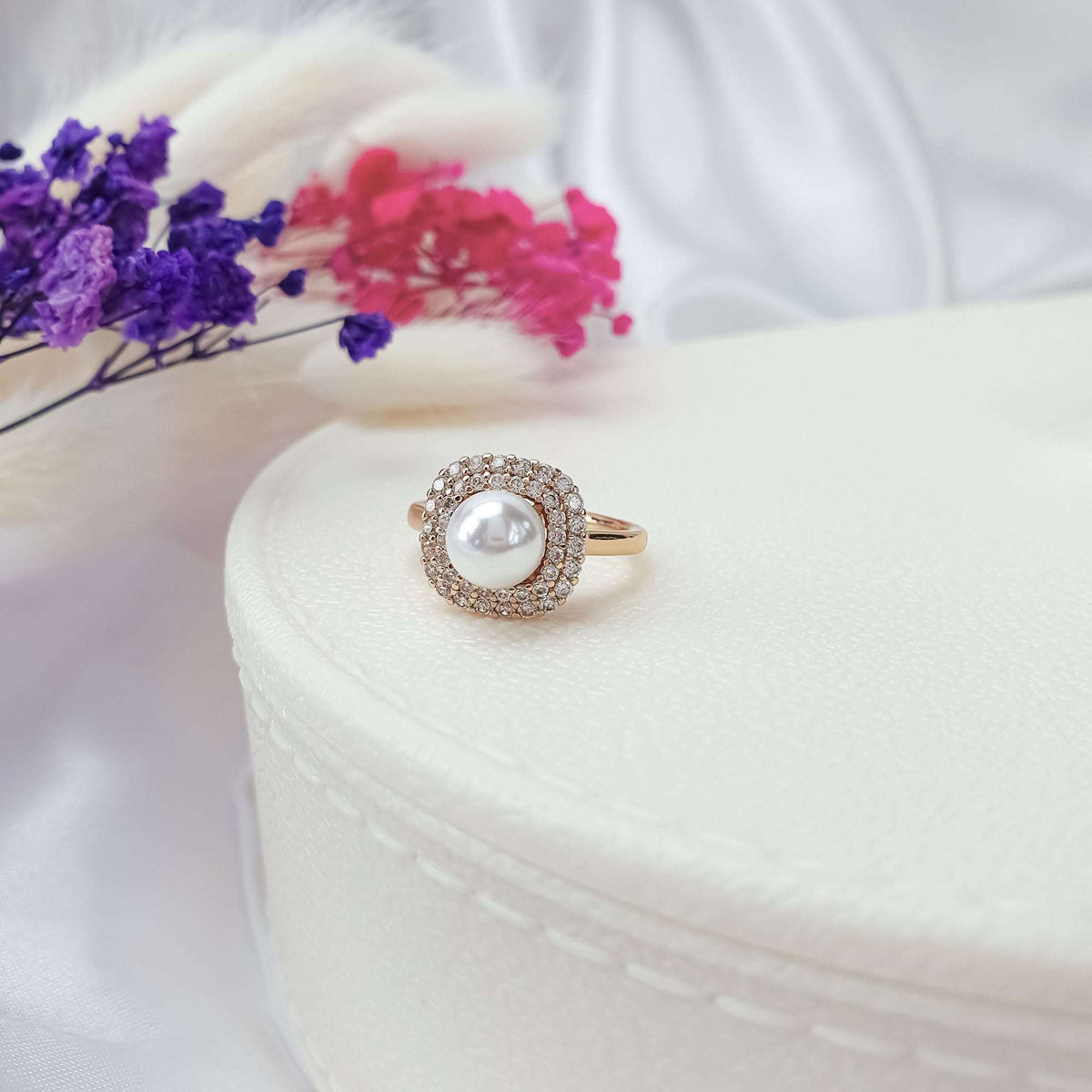 Gold-plated pearl ring, double cubic zirconia border, on a box by dried flowers