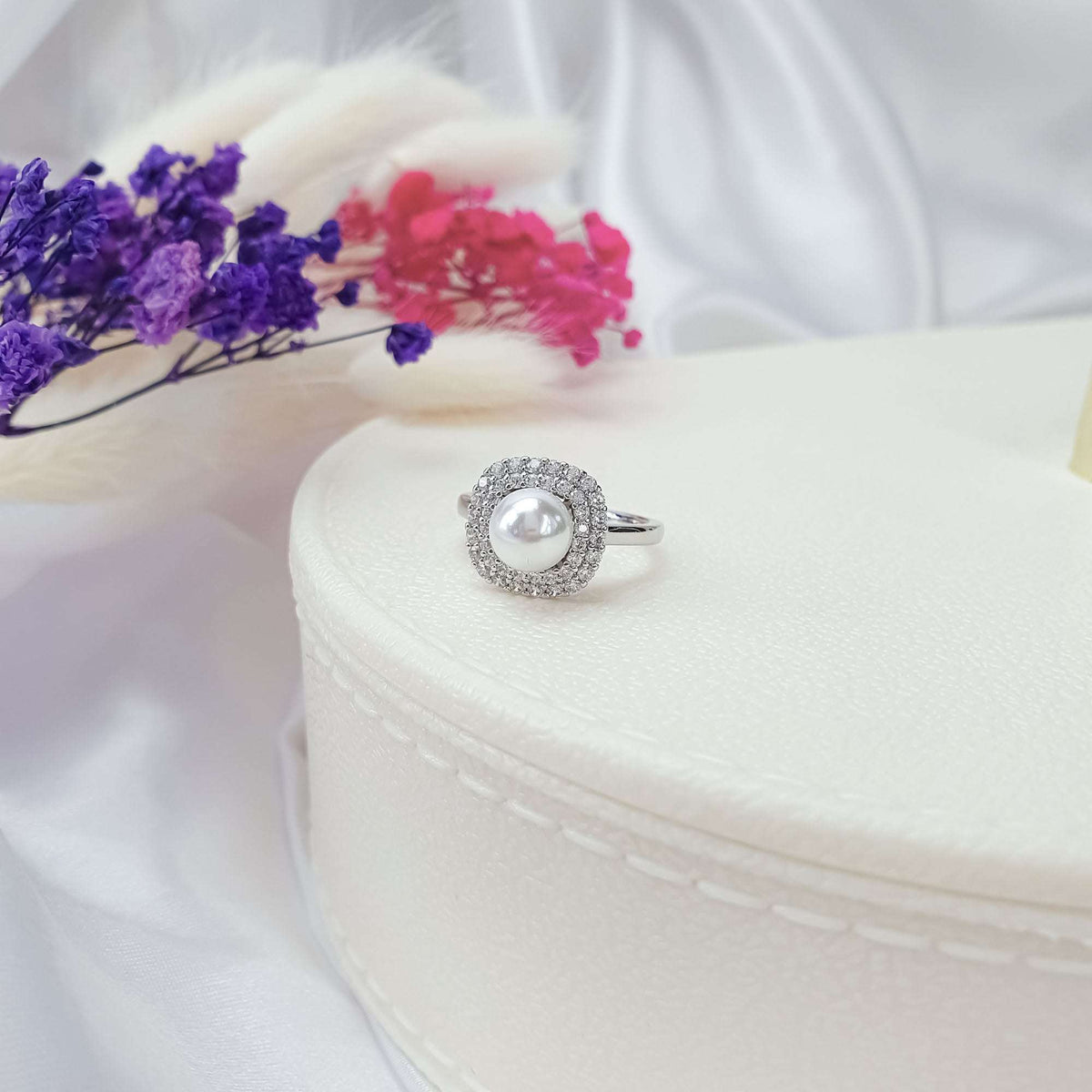 White pearl in a double cubic zirconia border, platinum-plated ring on a jewellery box