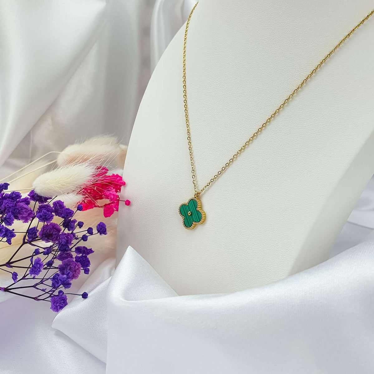 Green four-leaf pendant on a gold-plated chain displayed on a light stand