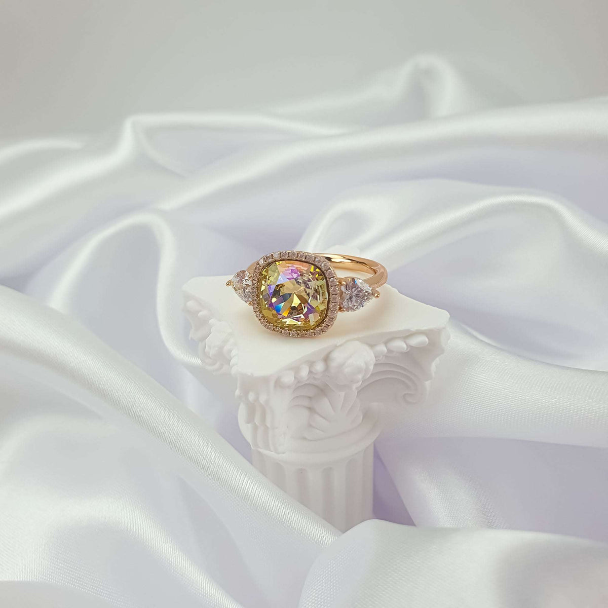 Ring on a white plaster column over satin, the stone shimmering in iridescent yellow